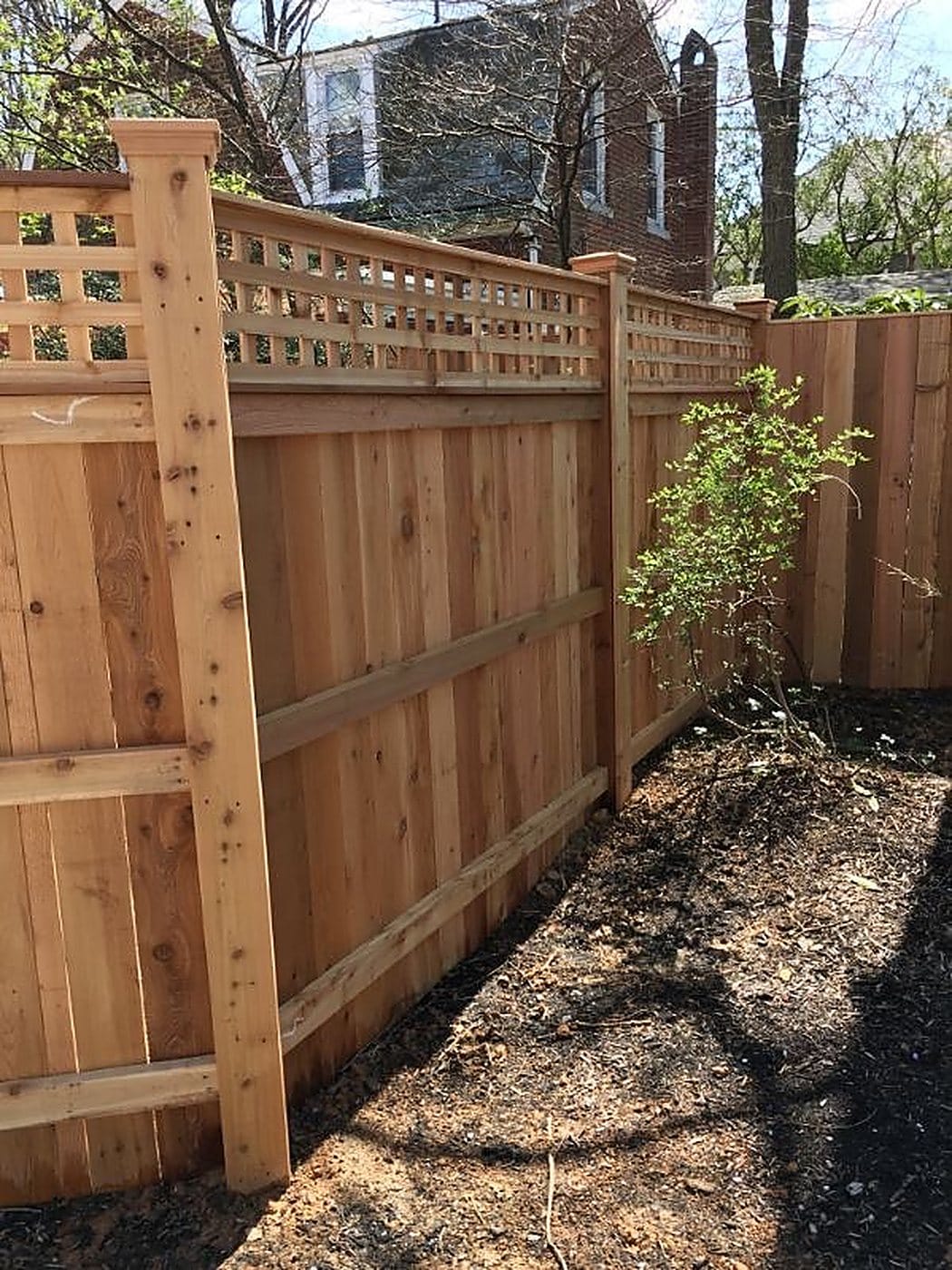 Cedar privacy fence with a lattice topper built along the side of a brick house