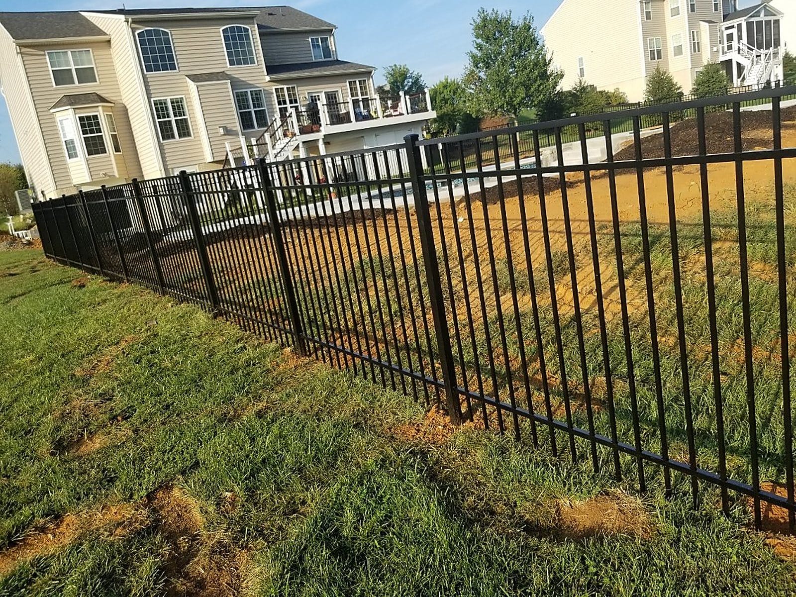 Black aluminum ornamental fence running downhill along a row of houses