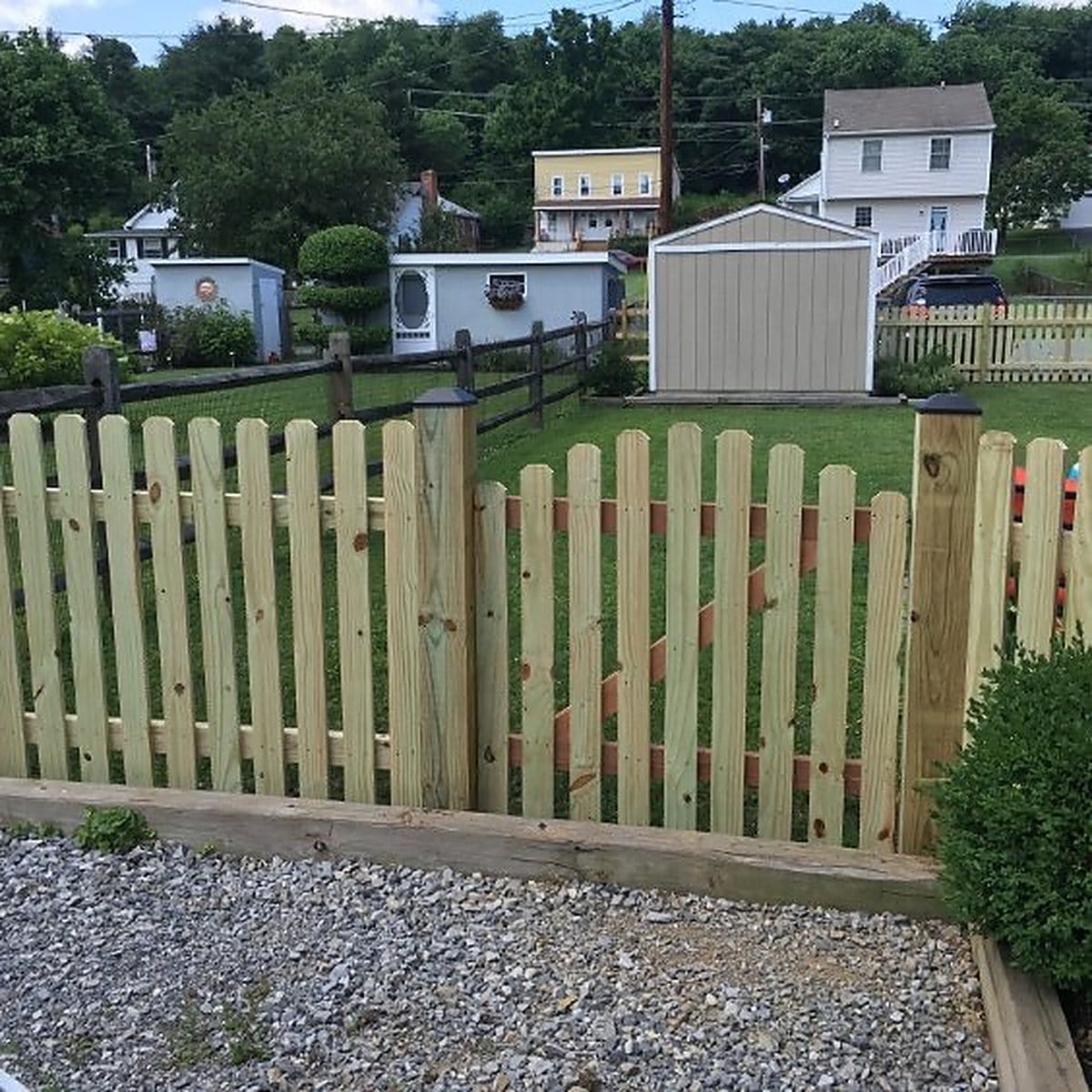 Dog ear wood picket fence and gate set against a gravel drive