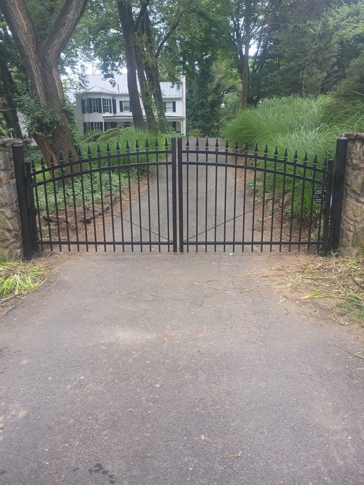 Arched black aluminum double entry gate on stone piers at the head of a private drive
